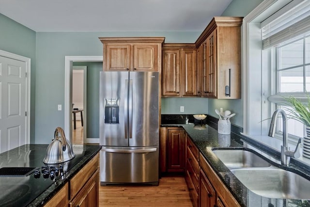 kitchen featuring black electric cooktop, a sink, wood finished floors, dark stone countertops, and stainless steel fridge