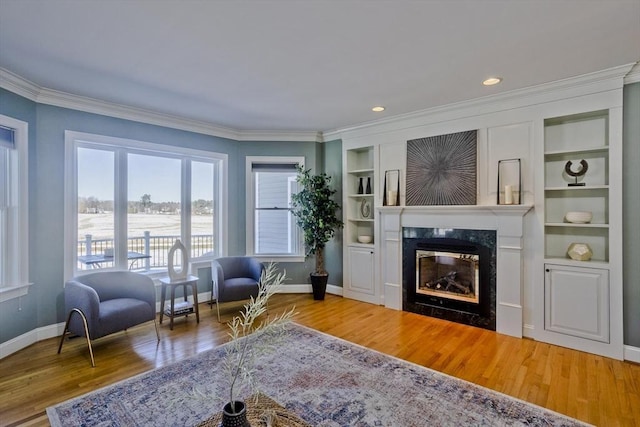 living area with baseboards, built in features, wood finished floors, and a glass covered fireplace