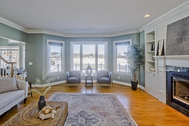 living room with baseboards, a tiled fireplace, wood finished floors, crown molding, and built in shelves