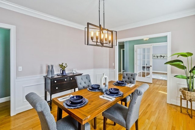 dining room with a wainscoted wall, french doors, ornamental molding, and light wood-type flooring