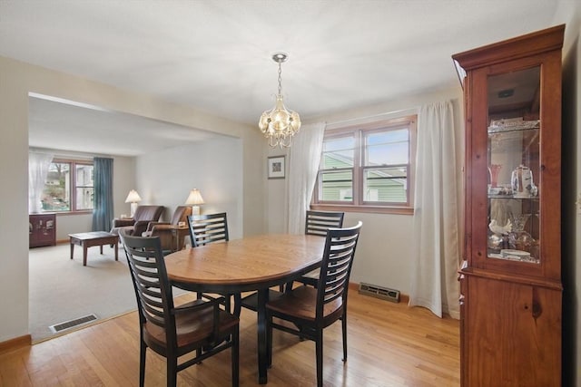 dining area featuring a chandelier, light wood-type flooring, visible vents, and baseboards