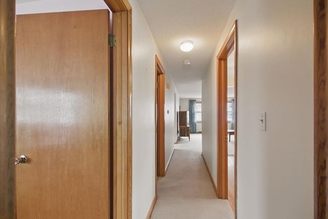 hall featuring light colored carpet, a textured ceiling, and baseboards