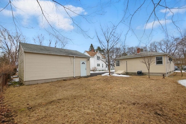 rear view of house with a yard, cooling unit, an outdoor structure, and a chimney