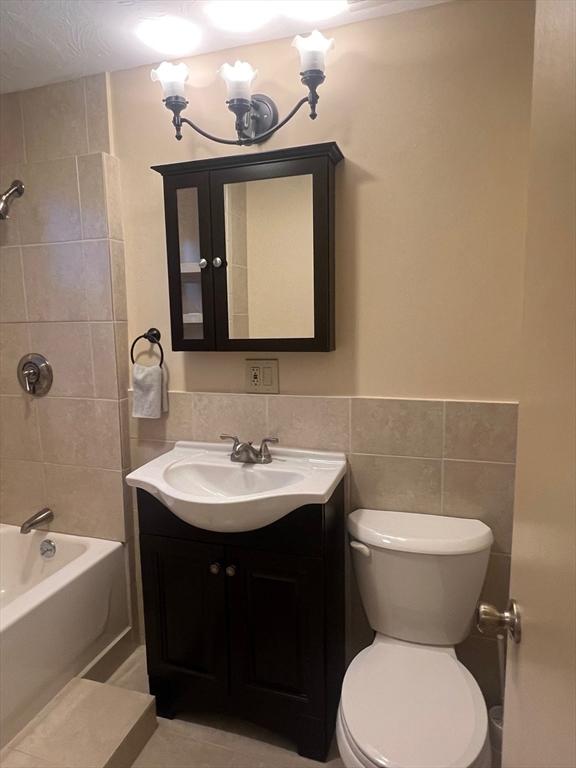 full bathroom with  shower combination, tile walls, vanity, and toilet