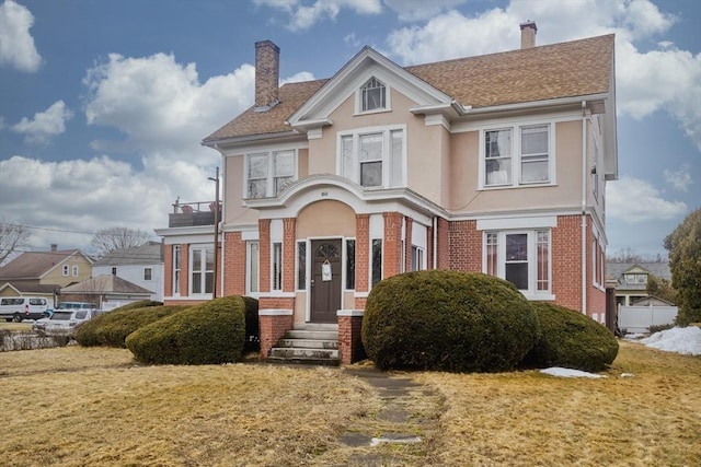 view of front of home featuring stucco siding, a front lawn, brick siding, and a chimney