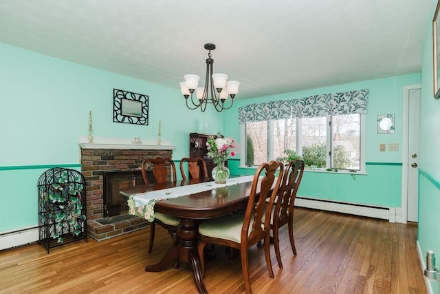 dining room featuring an inviting chandelier, hardwood / wood-style floors, a brick fireplace, and a baseboard heating unit