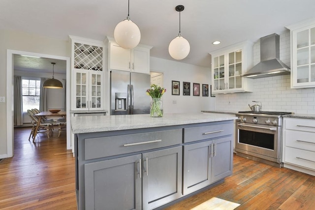 kitchen featuring white cabinets, gray cabinets, wall chimney exhaust hood, stainless steel appliances, and decorative backsplash