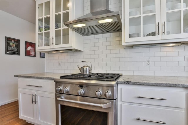 kitchen featuring wall chimney range hood, light stone countertops, baseboards, stainless steel range, and white cabinetry