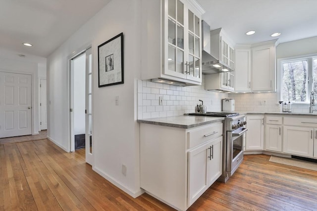 kitchen featuring stainless steel stove, light wood-style flooring, backsplash, and white cabinetry