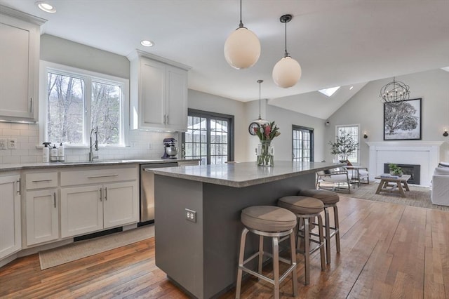 kitchen featuring decorative backsplash, a kitchen bar, a fireplace, dishwasher, and light wood-style floors