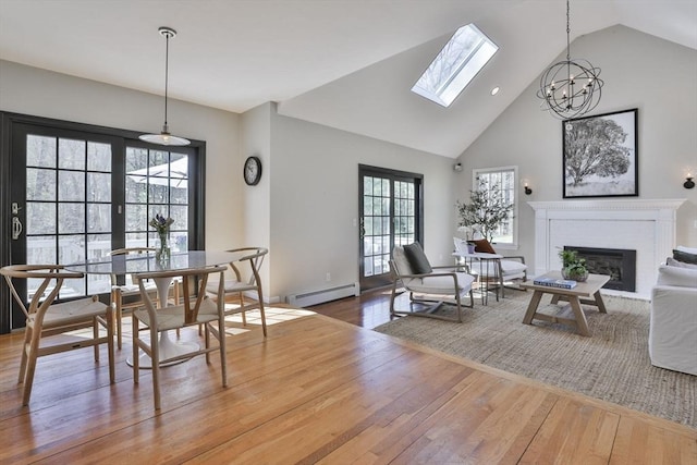 dining space with a skylight, a brick fireplace, wood finished floors, high vaulted ceiling, and a baseboard heating unit
