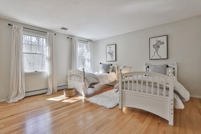 bedroom featuring baseboards, a baseboard radiator, wood-type flooring, and visible vents