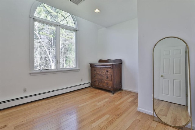 bedroom featuring light wood-style floors, multiple windows, a baseboard heating unit, and visible vents