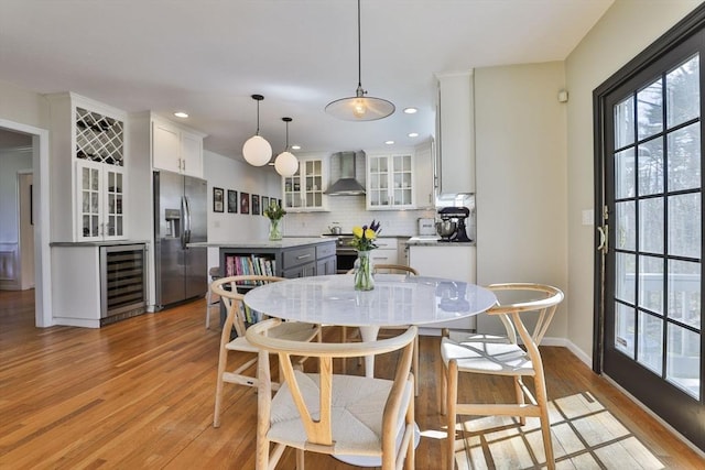dining room featuring light wood-style floors, baseboards, wine cooler, and a healthy amount of sunlight