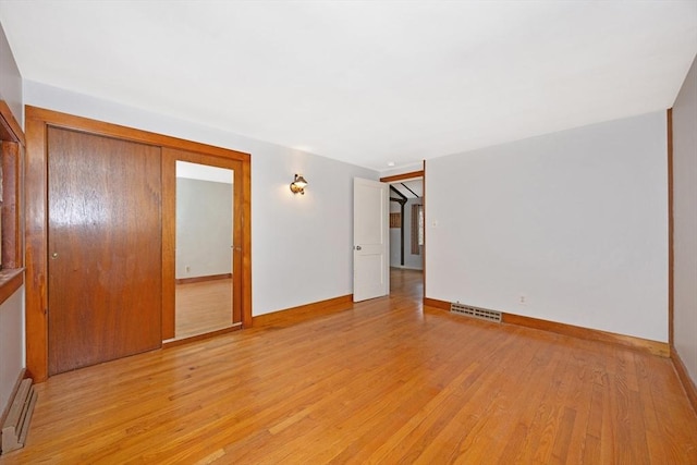 empty room with baseboards, a baseboard radiator, light wood-style flooring, and visible vents