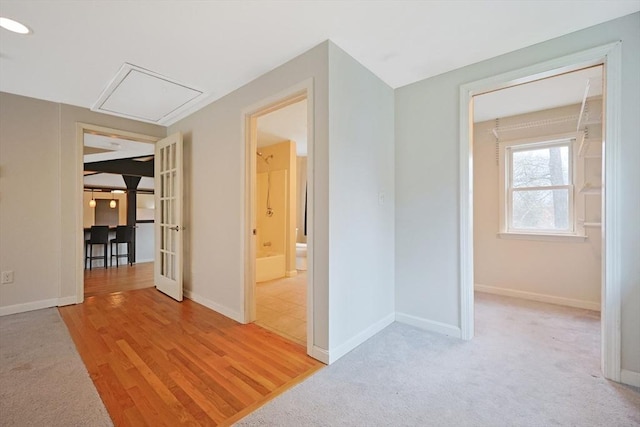 hallway featuring baseboards, light wood finished floors, and attic access