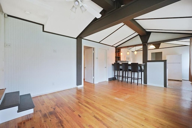 living area with baseboards, ceiling fan, lofted ceiling with beams, and light wood-type flooring
