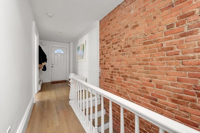 hall with wood finished floors, brick wall, baseboards, an upstairs landing, and baseboard heating