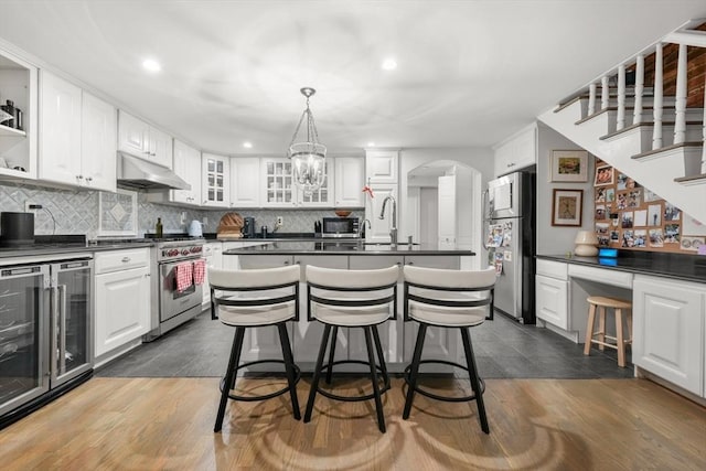 kitchen with beverage cooler, stainless steel appliances, under cabinet range hood, dark countertops, and recessed lighting