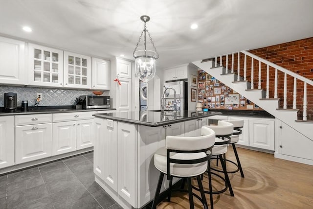 kitchen featuring stacked washing machine and dryer, appliances with stainless steel finishes, dark countertops, glass insert cabinets, and white cabinets
