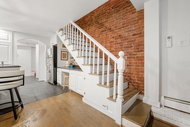 stairway featuring arched walkways, brick wall, wood finished floors, and baseboard heating