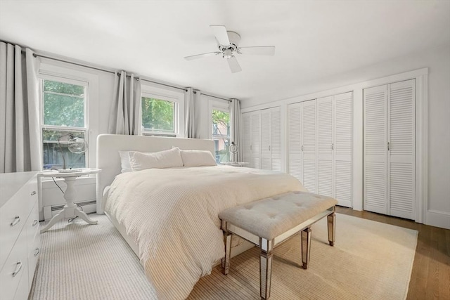 bedroom featuring light wood-style flooring, multiple closets, a baseboard heating unit, and ceiling fan