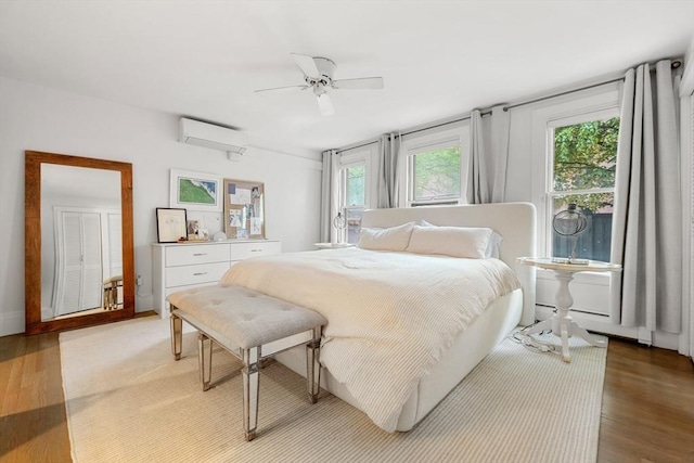 bedroom with a wall mounted air conditioner, light wood-type flooring, a baseboard heating unit, and a ceiling fan
