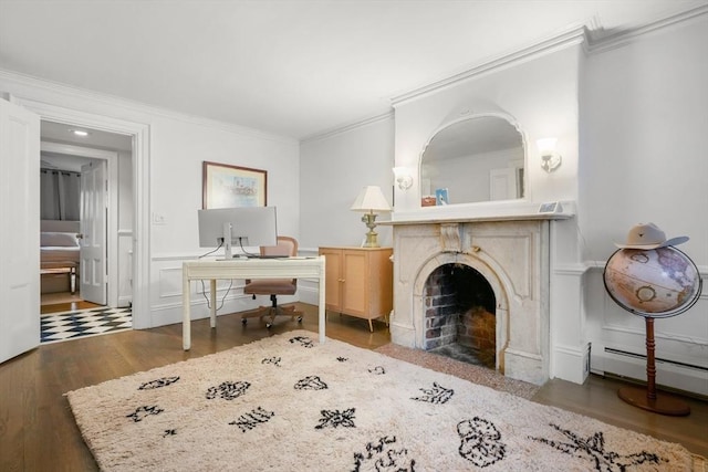 living area with ornamental molding, wood finished floors, a baseboard heating unit, a fireplace with flush hearth, and a desk