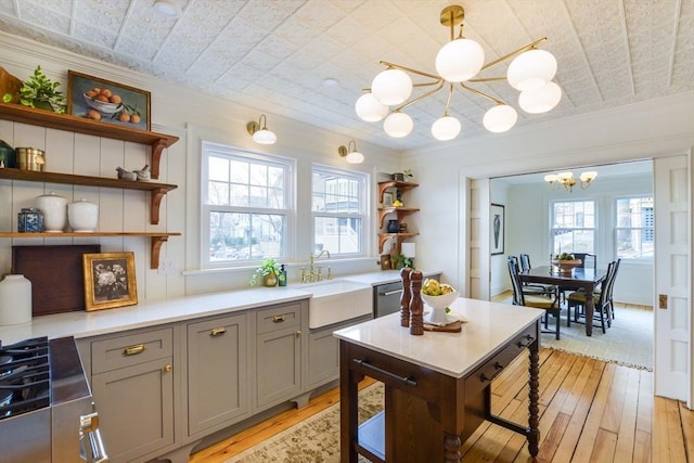 kitchen featuring open shelves, a sink, gray cabinetry, stainless steel dishwasher, and a notable chandelier