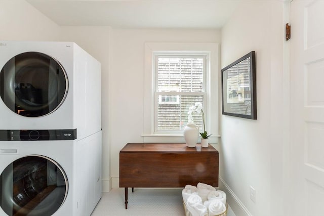 clothes washing area featuring baseboards, laundry area, and stacked washer / dryer