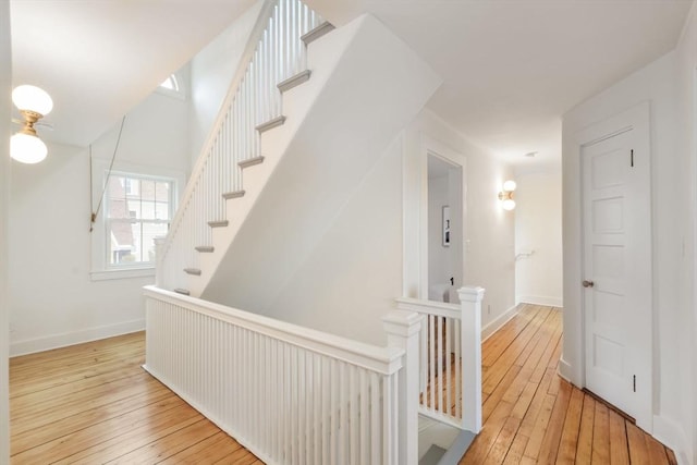 corridor with an upstairs landing, baseboards, and hardwood / wood-style floors