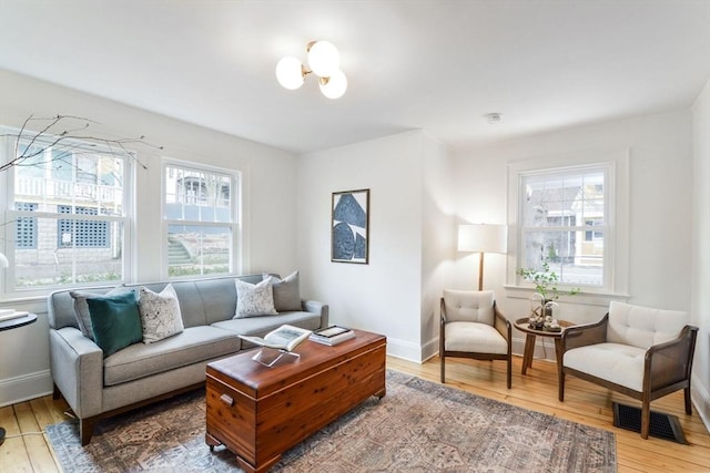 living room featuring hardwood / wood-style floors, baseboards, visible vents, and a chandelier