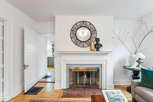 living room featuring visible vents, a fireplace with flush hearth, baseboards, and hardwood / wood-style flooring