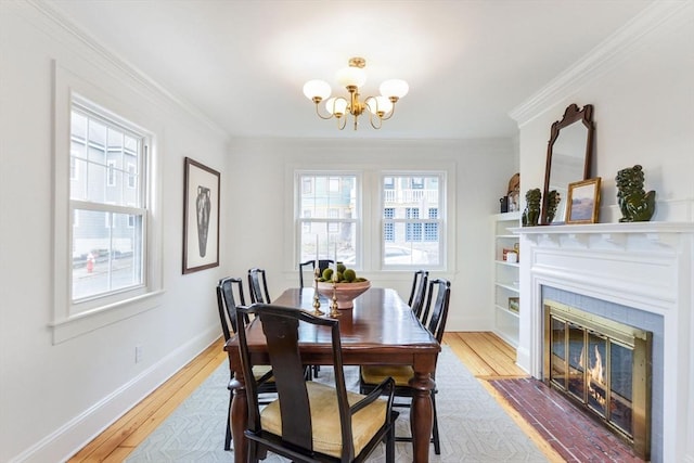 dining room featuring crown molding, a fireplace with flush hearth, baseboards, and light wood-type flooring