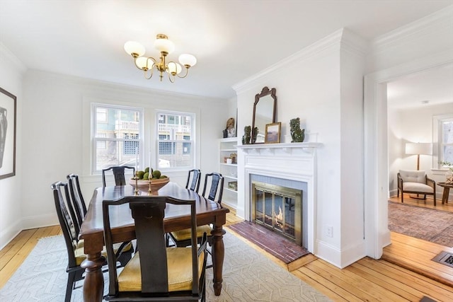 dining space with a glass covered fireplace, light wood-style flooring, ornamental molding, and a chandelier