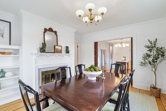 dining space featuring light wood finished floors, a glass covered fireplace, an inviting chandelier, and ornamental molding