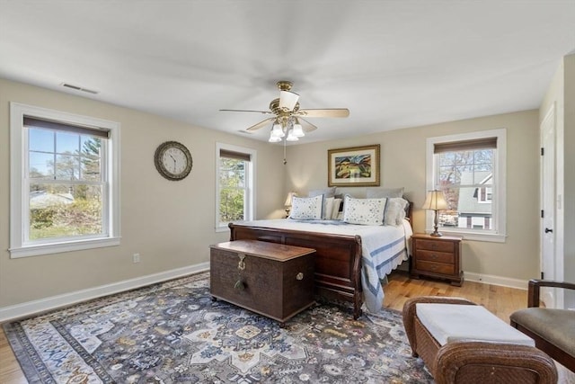 bedroom featuring baseboards, visible vents, multiple windows, and wood finished floors