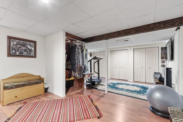 exercise room featuring baseboards, visible vents, wood finished floors, and a paneled ceiling
