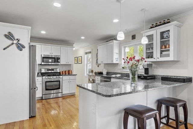 kitchen featuring crown molding, appliances with stainless steel finishes, dark stone countertops, a peninsula, and glass insert cabinets