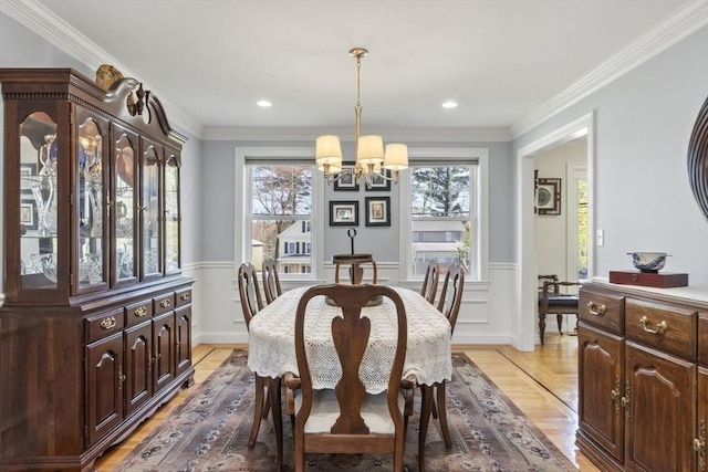 dining room with an inviting chandelier, ornamental molding, light wood-style floors, and wainscoting
