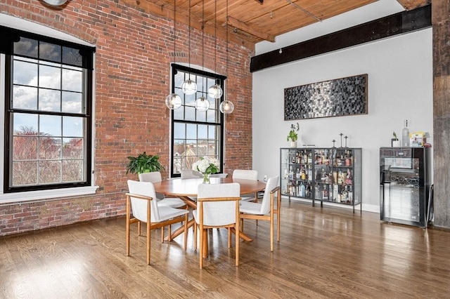 dining space featuring wood ceiling, wood finished floors, brick wall, and a towering ceiling