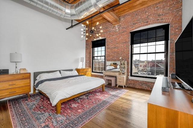 bedroom with wood finished floors, brick wall, beamed ceiling, a high ceiling, and a notable chandelier