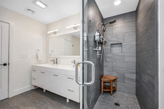 bathroom with baseboards, visible vents, a tile shower, and vanity