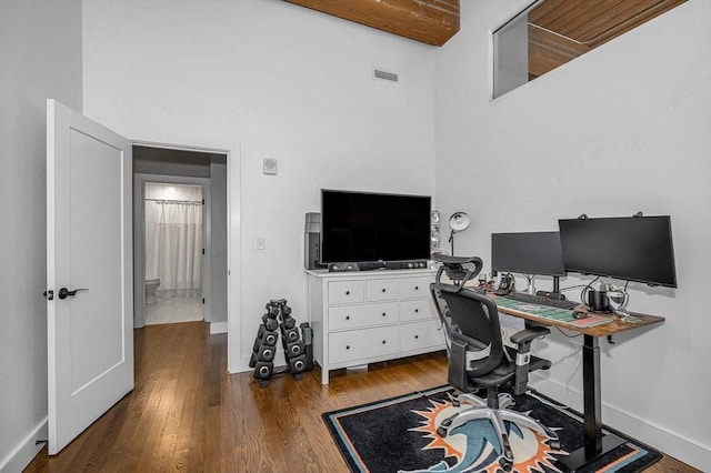 office area featuring baseboards, wood finished floors, and a towering ceiling