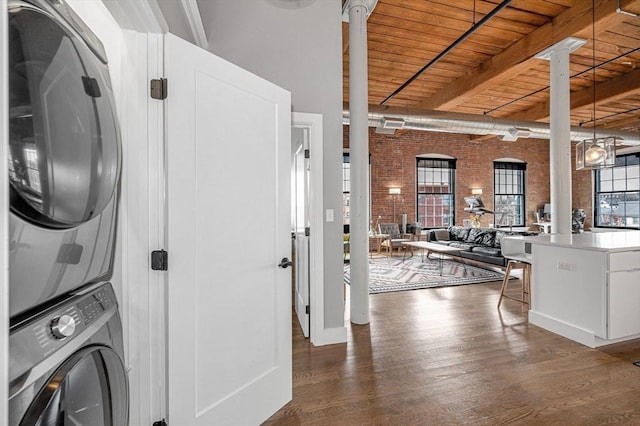 washroom featuring laundry area, wood finished floors, brick wall, stacked washing maching and dryer, and wooden ceiling