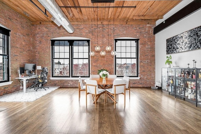 dining room with wood finished floors, brick wall, and a healthy amount of sunlight