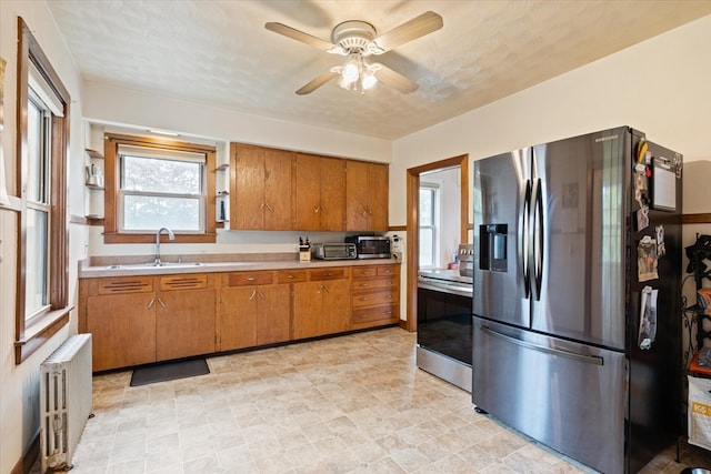 kitchen with ceiling fan, sink, radiator heating unit, a textured ceiling, and appliances with stainless steel finishes