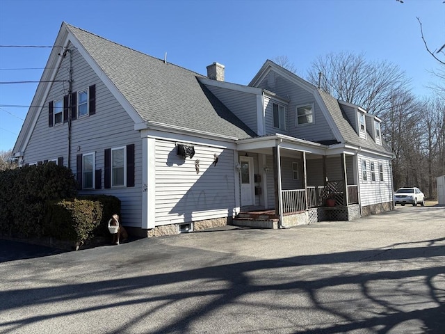 view of front of property featuring a gambrel roof, a chimney, a porch, and roof with shingles