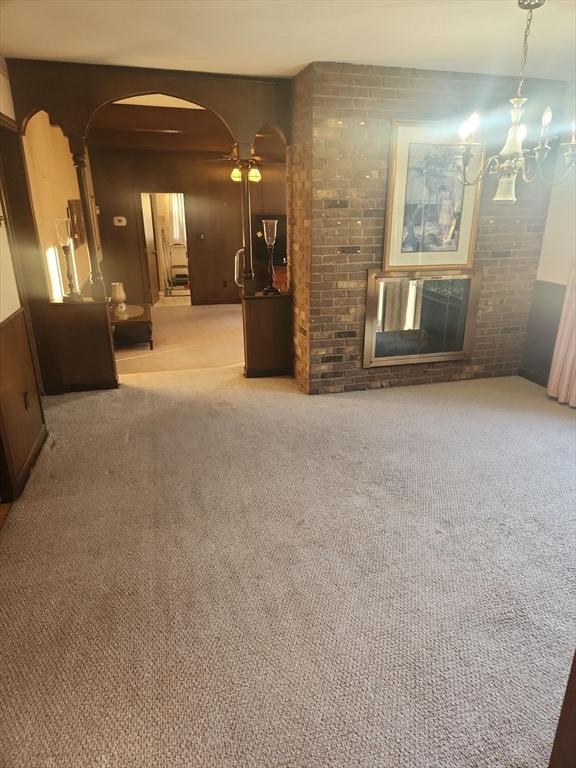 unfurnished living room featuring ceiling fan with notable chandelier and light carpet