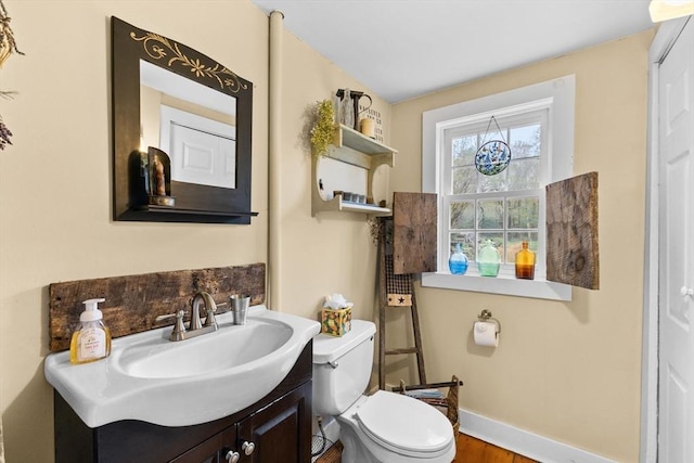 bathroom with toilet, vanity, baseboards, and wood finished floors